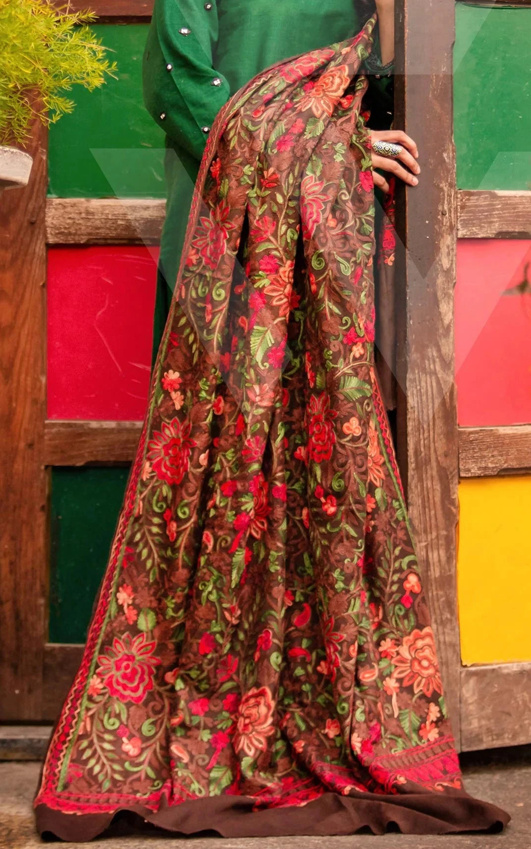 Woman in a green and floral dress standing in front of a colorful wooden door.