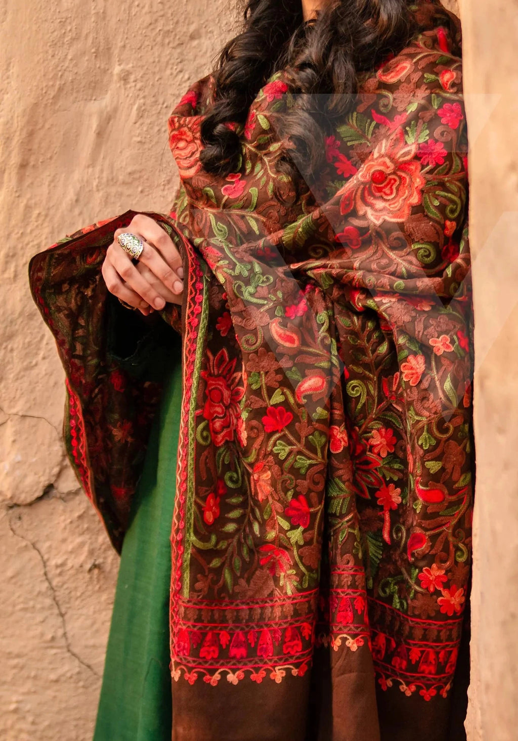 Woman wearing a floral embroidered shawl against a beige wall