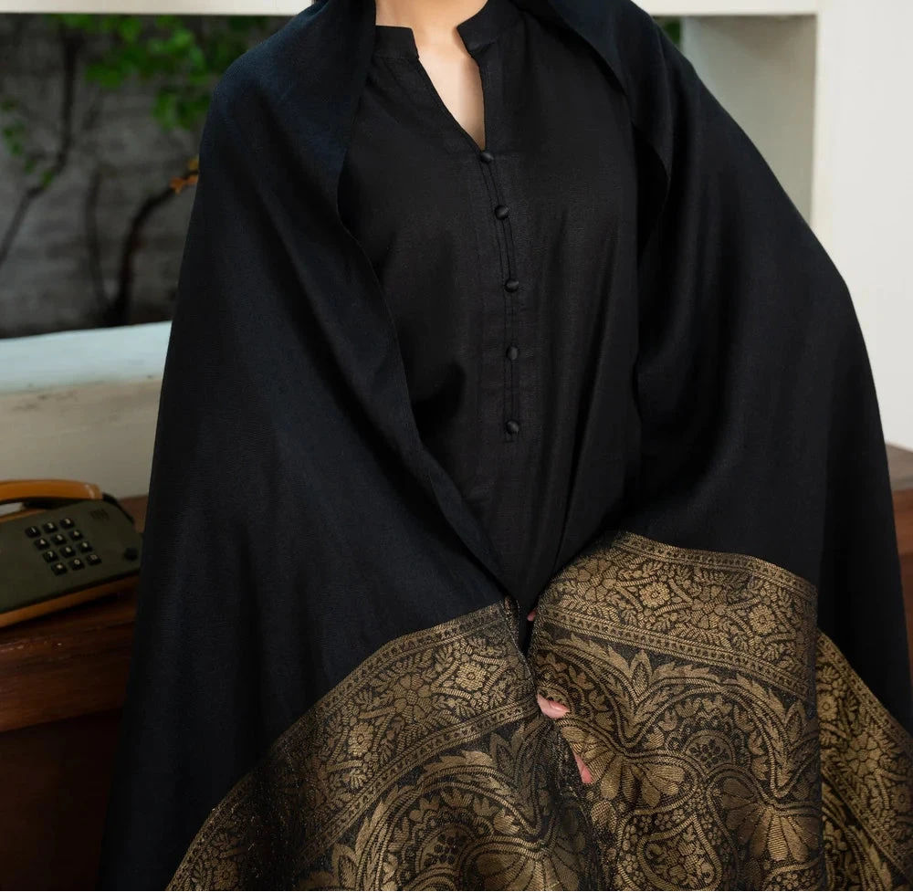 Woman wearing a black shawl over a patterned skirt with a blurred outdoor background