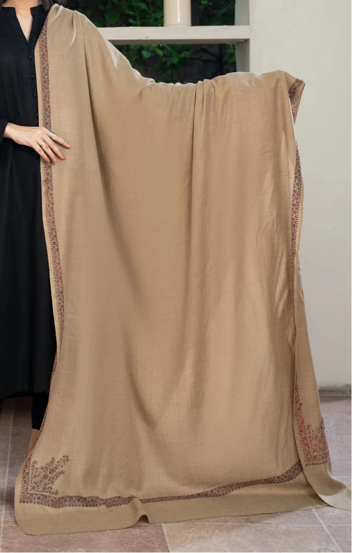 Woman holding a beige dupatta with a wooden cabinet and greenery in the background