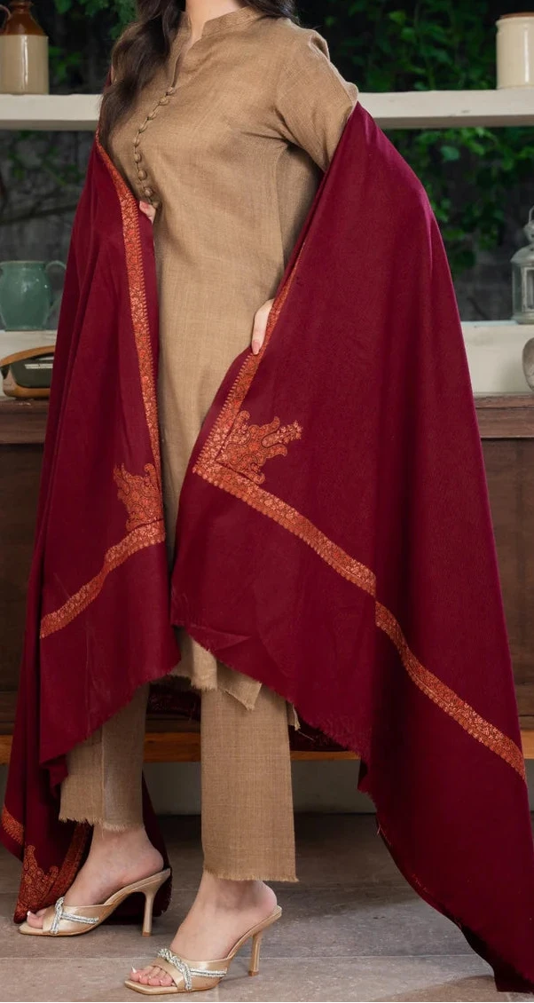 Woman in beige outfit with a red shawl draped over her shoulders, standing indoors.