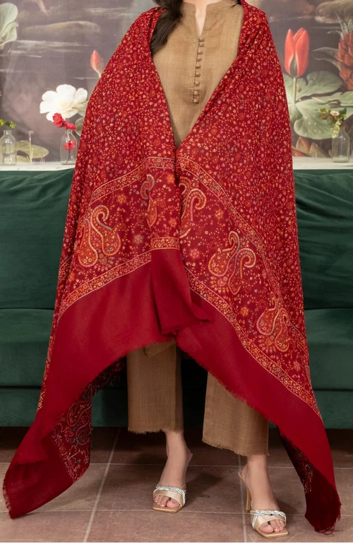 Woman wearing a red patterned shawl over a beige outfit in a decorated room.