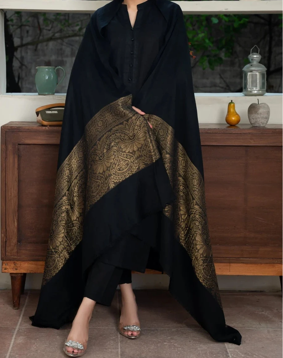 Woman wearing a black and gold dress with a patterned design, standing indoors.