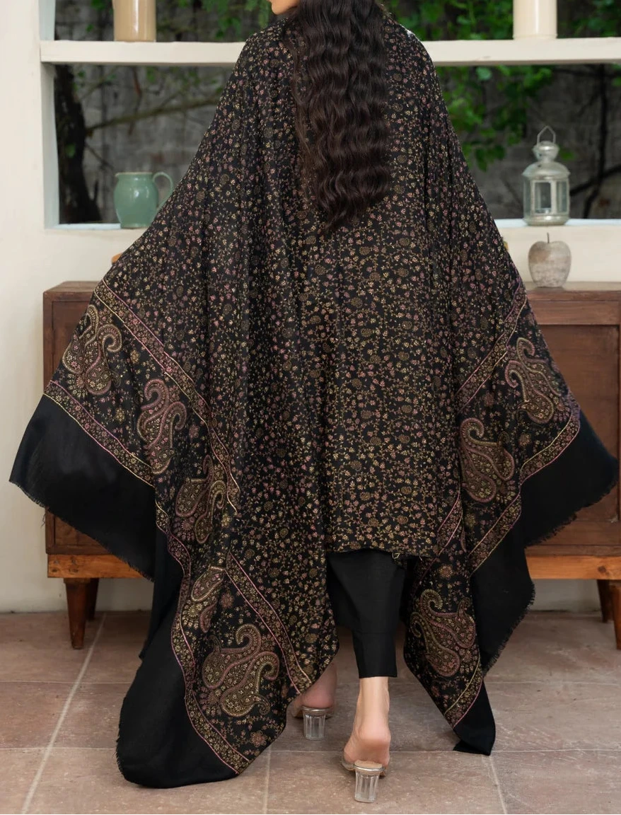 Woman wearing a patterned shawl in a room with a wooden cabinet and greenery outside.