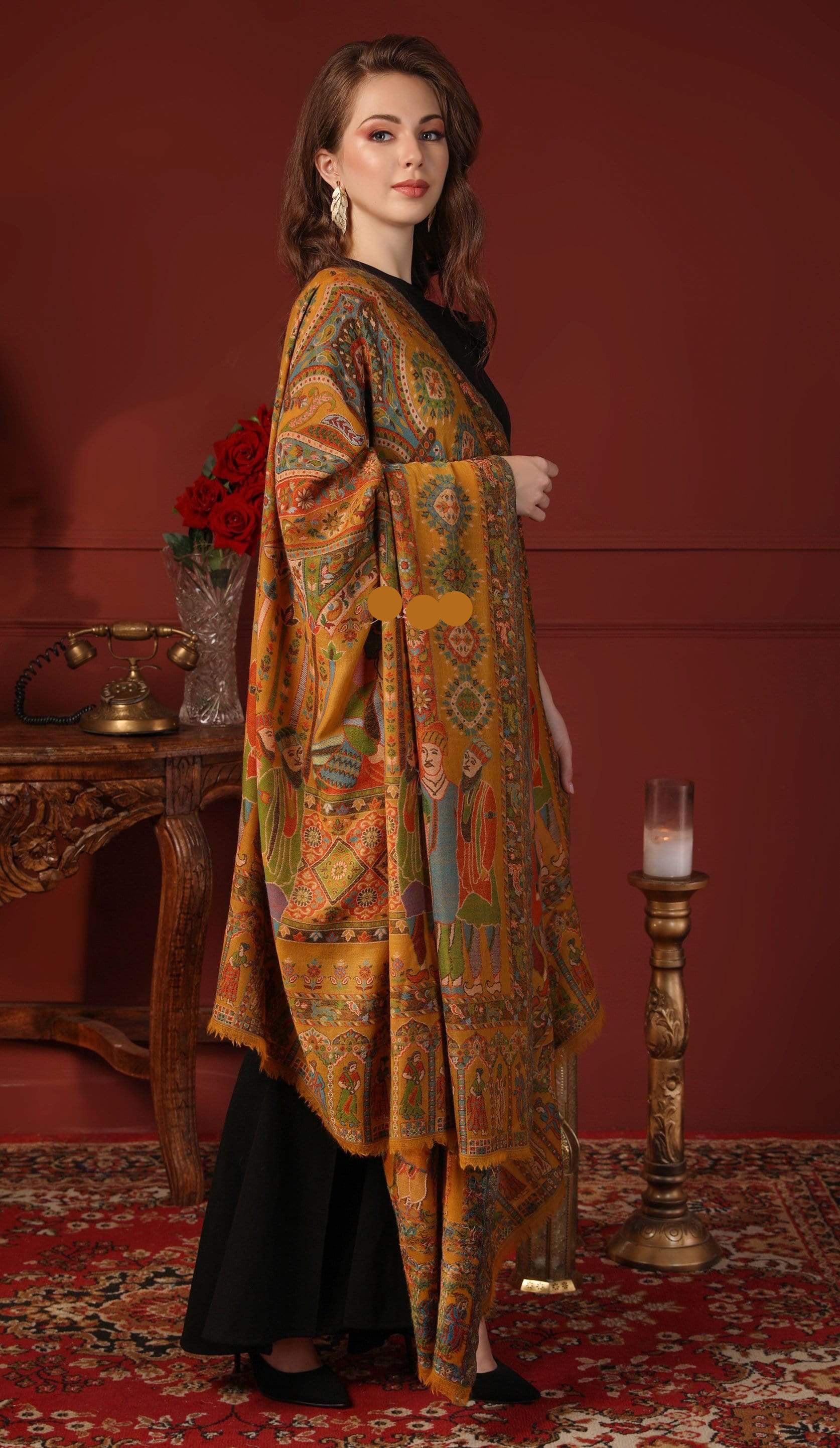 Woman wearing a patterned shawl over a black outfit in a decorative setting with a red wall and candle.