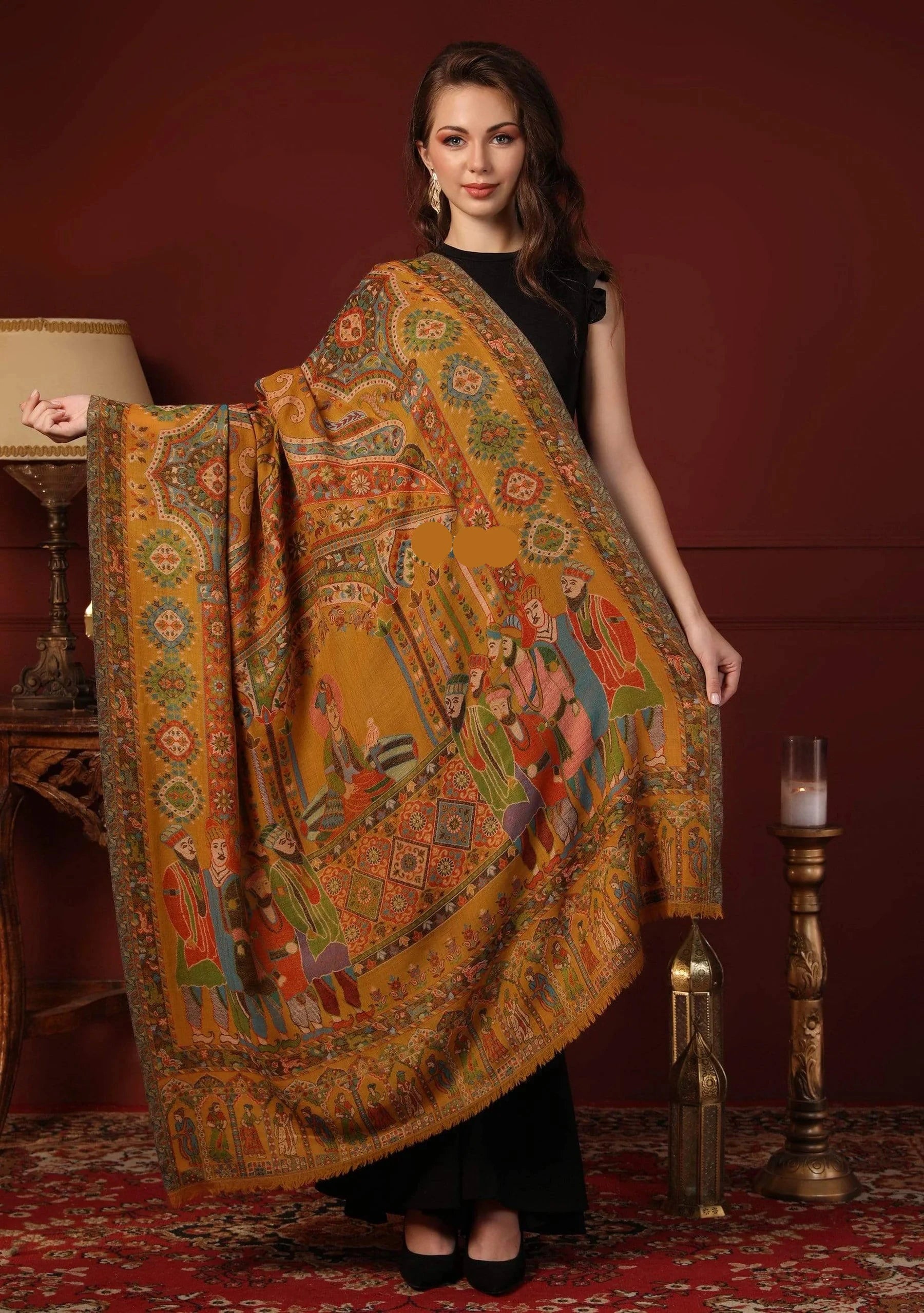 Woman holding a large, colorful patterned scarf in a room with a lamp and candle on a table.